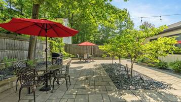 An outdoor patio with a table and chairs, a red umbrella, and a wooden fence.