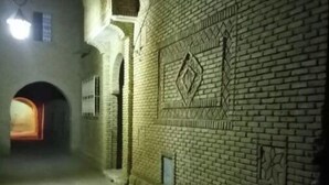 A narrow alleyway with a brick wall featuring geometric patterns, a small window, and a light source at the end of the alley. - Dar Naftah, la belleza del sur de Túnez, una perla (Nefta)