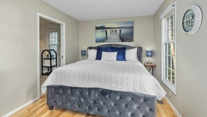 Une chambre à coucher avec un grand lit, un tableau au-dessus du lit, une fenêtre donnant sur un beau paysage et une porte menant à une autre pièce.