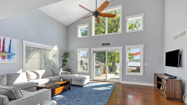 A spacious living room with a ceiling fan, large windows, a flat-screen TV, and a wooden entertainment center. - Spacious 5BR, 3BA Waterfront Home w/Fenced Backyard & Private Boat Dock (Saugatuck)