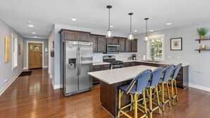 A modern kitchen with a central island, stainless steel appliances, and bar stools. - Spacious 5BR, 3BA Waterfront Home w/Fenced Backyard & Private Boat Dock (Saugatuck)