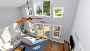 A modern living room with a sectional sofa, a ceiling fan, and a view of a deck through large windows. - Spacious 5BR, 3BA Waterfront Home w/Fenced Backyard & Private Boat Dock (Saugatuck)