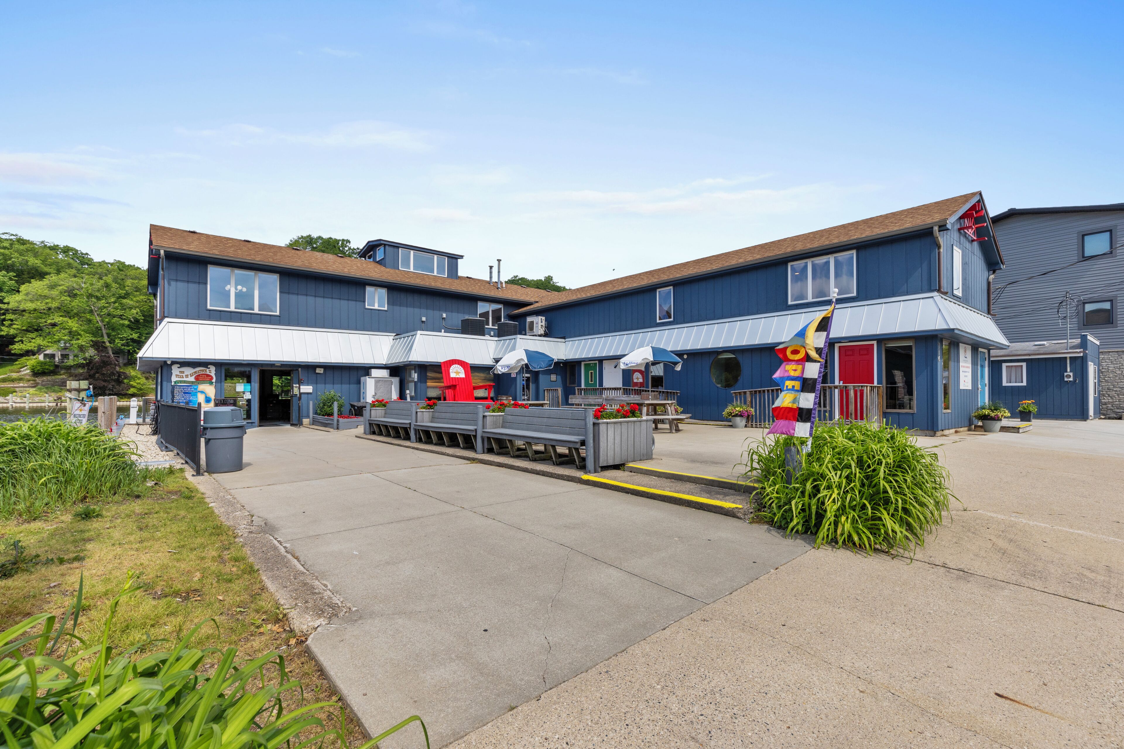 A two-story building with a blue exterior, a covered outdoor seating area, and a flagpole with a colorful flag.