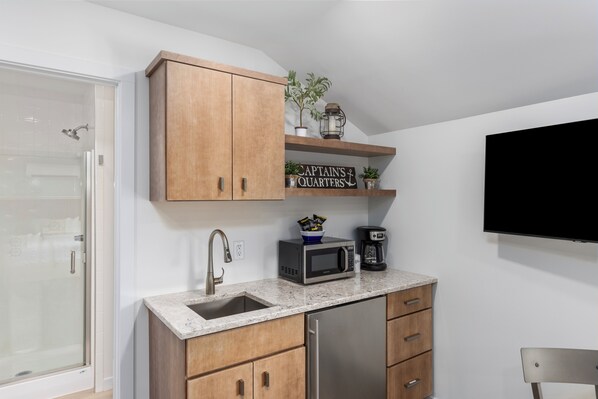Une cuisine avec des meubles en bois, un réfrigérateur en acier inoxydable, un four à micro-ondes, une machine à café et une pancarte sur laquelle on peut lire : « CABINE DU CAPITAINE ».