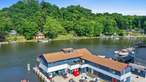 A lakeside building with a dock, outdoor seating, and a view of the lake and forested hills.