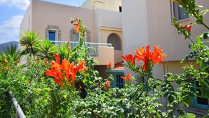 A building with a balcony, surrounded by greenery and red flowers. - Lotus Studios (Hersonissos)