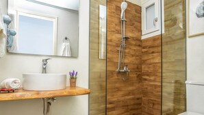 A modern bathroom with a glass-enclosed shower, a wooden vanity, a white sink, and a toilet. - Lotus Studios (Hersonissos)