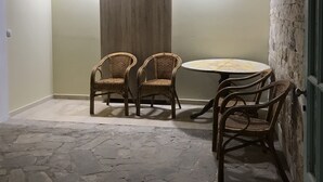 A room with a stone floor, wicker chairs, a round table, and a wooden door. - Lotus Studios (Hersonissos)