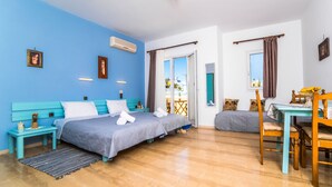 A bedroom with a bed, bedside tables, a desk, and a chair. There is a window with curtains, a door leading to another room, and a balcony visible through the window. - Lotus Studios (Hersonissos)