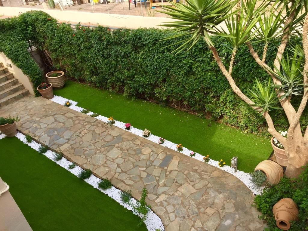 A landscaped garden with a stone pathway, green hedges, and potted plants.