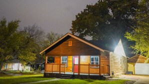 Une cabane en bois avec un porche à l’avant, un garage et un grand arbre en arrière-plan.
