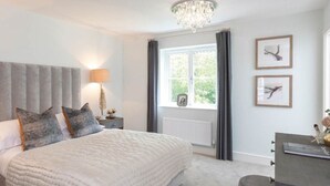 A bedroom with a large bed, a bedside table with a lamp, a chandelier, a window with curtains, and framed pictures on the wall. - Wonderful Country Side Home, Winchester near River Test, Winchester Cathedral 6k (Winchester)