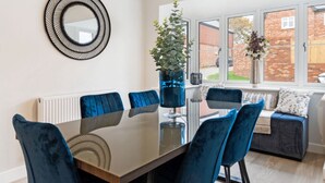 A dining area with a glass table, blue velvet chairs, a modern pendant light, and a view of a brick building outside. - Wonderful Country Side Home, Winchester near River Test, Winchester Cathedral 6k (Winchester)