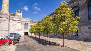 A paved courtyard with a row of trees, a stone building with arched windows, and parked cars. - Luxury 2 bed Apartment Mount Wise Plymouth Parking (Plymouth)
