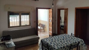 A room with a sofa, a table with a patterned tablecloth, a laptop on a side table, and a window with bars.