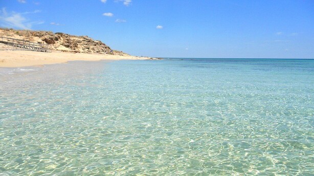 A clear beach with shallow water, sandy shore, and rocky outcrops.
