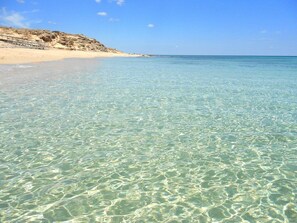 A clear beach with shallow water, sandy shore, and rocky outcrops. - Villa Acqua Dolce, just 40 meters from the sea (Acquadolce Cirenaica)