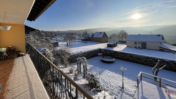 A balcony with a view of a snow-covered yard, houses, and distant hills.