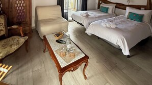 A cozy room with wooden beams, two beds with white linens, a wooden cabinet, a marble coffee table, and a painting on the wall.