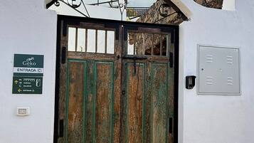 Entrada de hotel con una reja metálica, un muro de piedra y un cartel que indica la entrada.