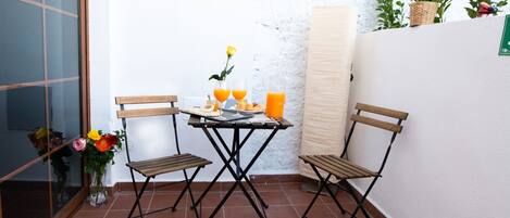 Un petit espace patio avec une table et deux chaises, un vase rempli de fleurs et une plante en pot.