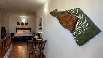 Hotelkamer met een bed, een bureau en stoelen. Er hangt een kunstwerk aan de muur en er is een lamp.