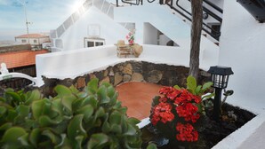 A white building with a stone foundation, a staircase, and a small garden with red flowers.