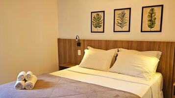 En snyggt bäddad säng med ett grått täcke, vita kuddar och hoprullade handdukar på sidan. En luftkonditioneringsenhet är monterad på väggen ovanför sängen.