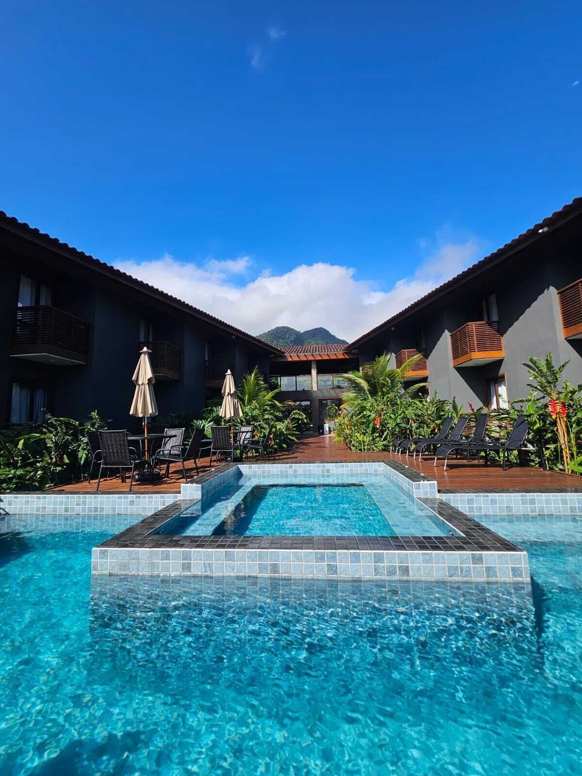 A hotel with a swimming pool, outdoor seating, and a mountain view.