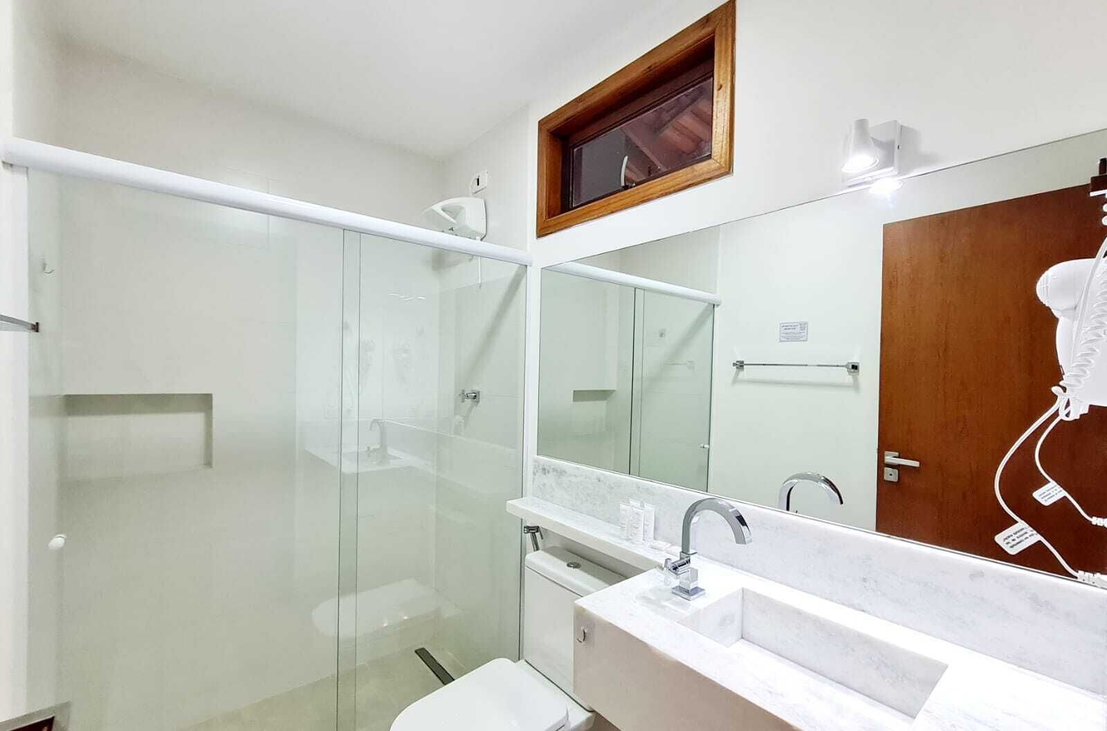Um banheiro moderno com box de vidro, um espelho grande e porta de madeira.