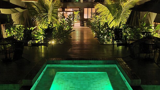 Un área de piscina con piso de baldosas y una fuente de agua iluminada en verde.