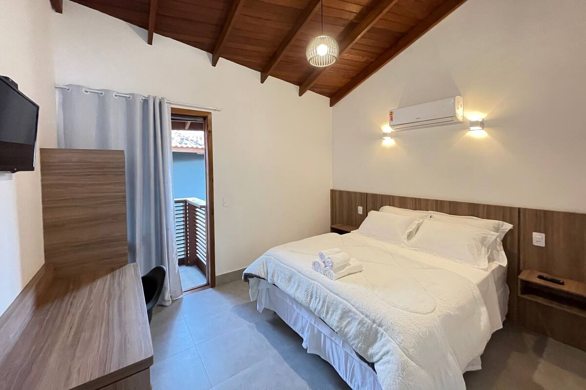 Un dormitorio con techo de madera, cama con ropa de cama blanca, televisor en la pared y aire acondicionado.