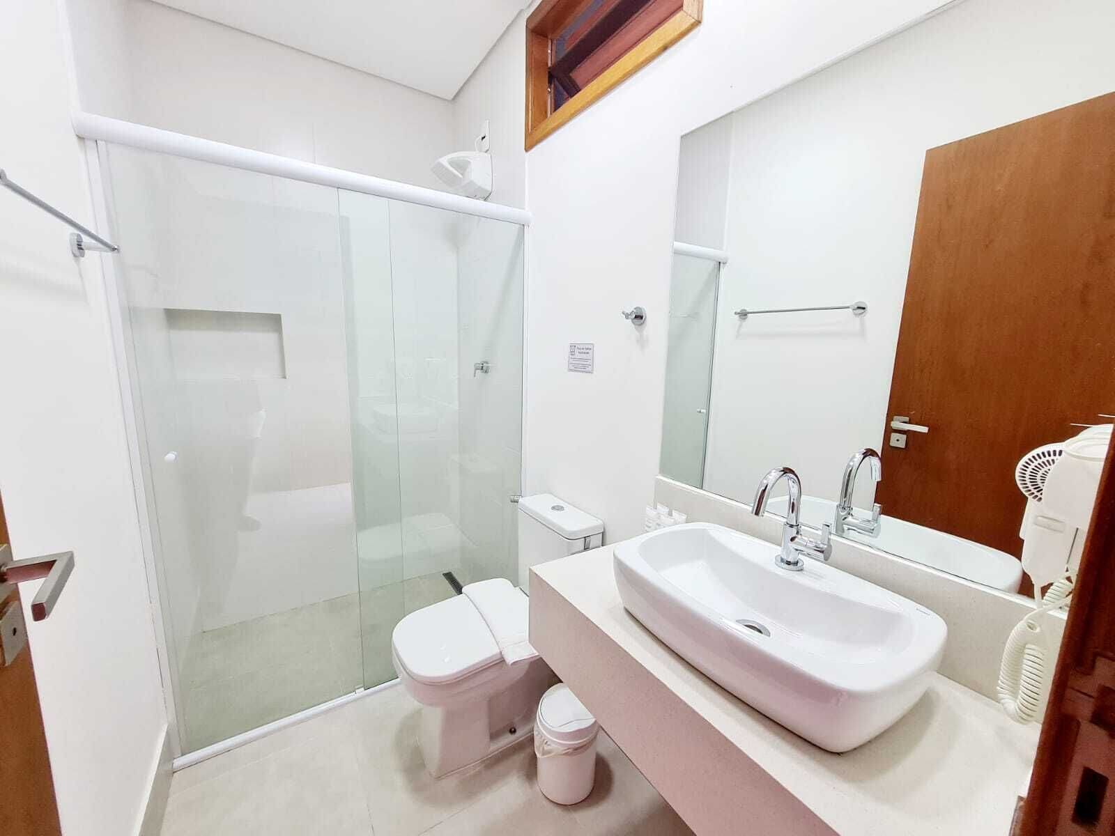 A modern bathroom with a glass-enclosed shower, a white toilet, and a large sink with a mirror above it.