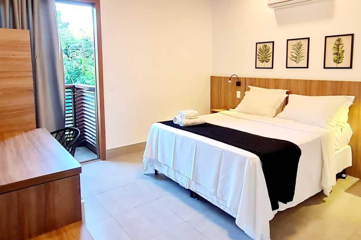Habitación de hotel con techo de madera, cama con ropa blanca, escritorio y ventana con cortinas.