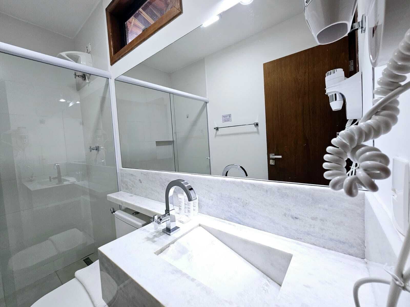 Une salle de bain moderne avec une douche à l’italienne en verre, un lavabo blanc doté d’un plan de toilette en marbre et un grand miroir au-dessus du lavabo.
