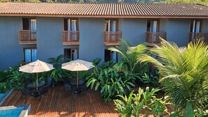 Un hotel con terraza que cuenta con piscina, asientos al aire libre y abundante vegetación.