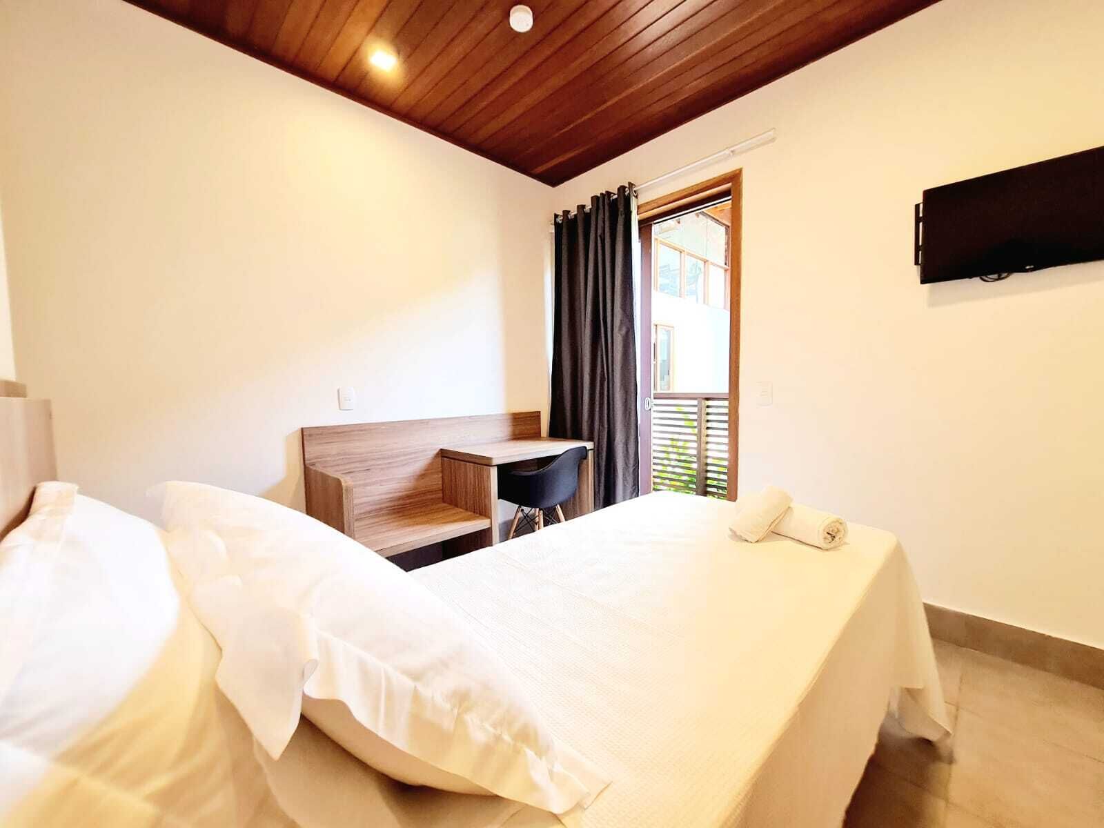 A hotel room with a wooden ceiling, a bed, a desk, and a window with curtains.