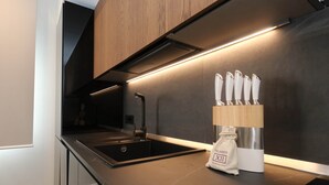 A modern kitchen with a black induction cooktop, a stainless steel sink, and a wooden knife block with knives. - Luxurious, Fully Renovated 2BR Townhouse with Terrace in Central Olbia. (Olbia)