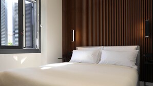 Un dormitorio moderno con una cama grande, un panel de madera en la pared y una ventana con persianas.