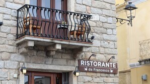 A stone building with a balcony featuring wrought iron railings and wooden chairs. A sign reads "RISTORANTE da Francesco." - Hidden GEM- luxurious holiday STUDIO Garibaldi-for couples (Olbia)