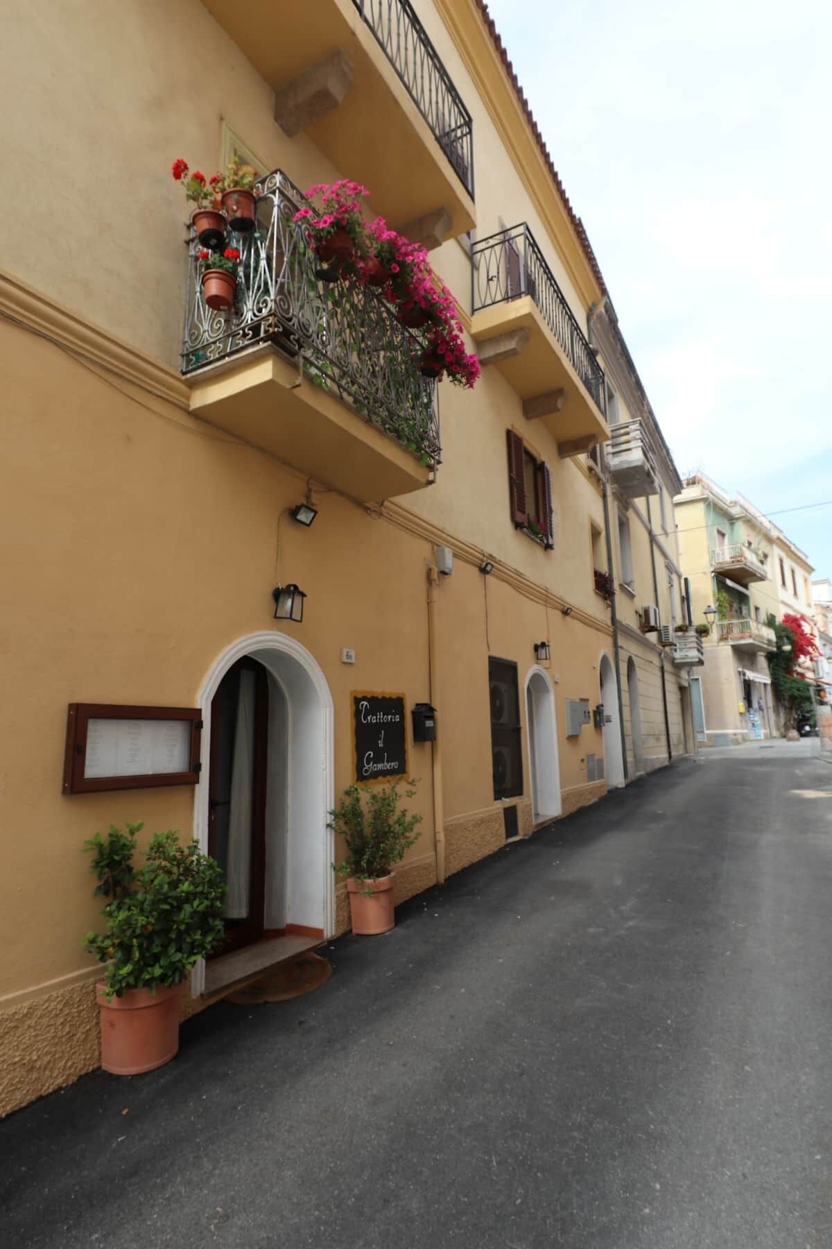 A building with a sign reading "Trattoria il Gambero" and a balcony with potted plants and flowers.