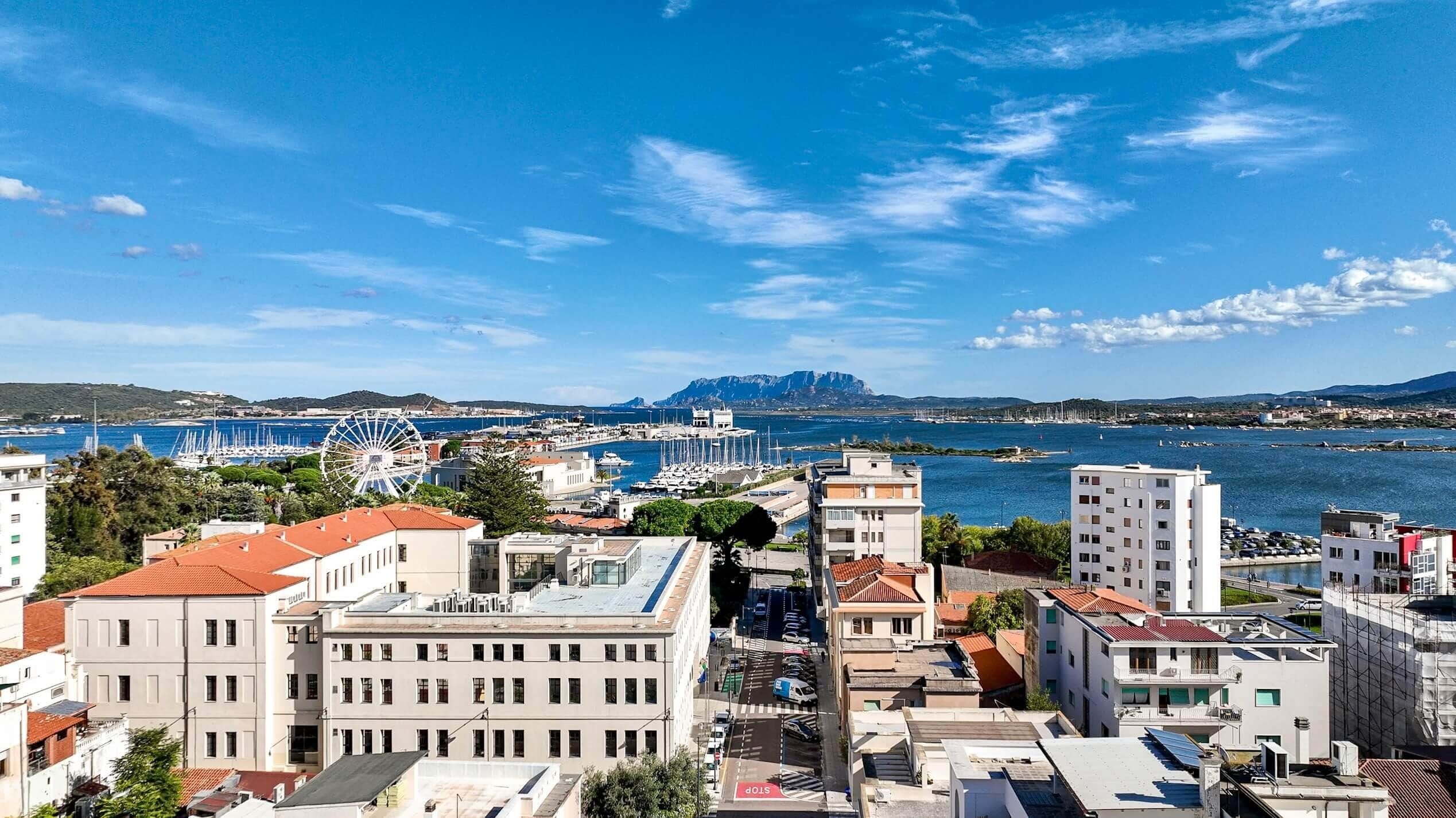 A coastal cityscape with a marina, buildings, and a clear sky.