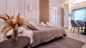 Een moderne hotelkamer met een groot bed, een nachtkastje met een vaas gedroogde bloemen, een houten paneelwand en uitzicht op de eetruimte.