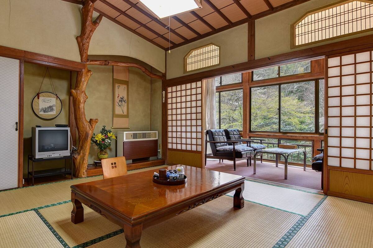 A traditional Japanese room with tatami flooring, a low table, a sofa, and sliding doors with a view of greenery.