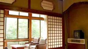 Una habitación tradicional japonesa con suelo de tatami, una mesa baja, un sofá y un televisor.