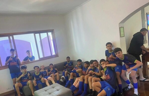 A group of people seated on a couch in a room with a large window and a mirror on the wall. - Youse Hostel and Hotel  (São Paulo)