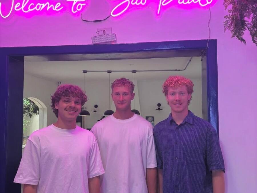 Three individuals standing in front of a neon sign that reads 'Welcome to São Paulo.'