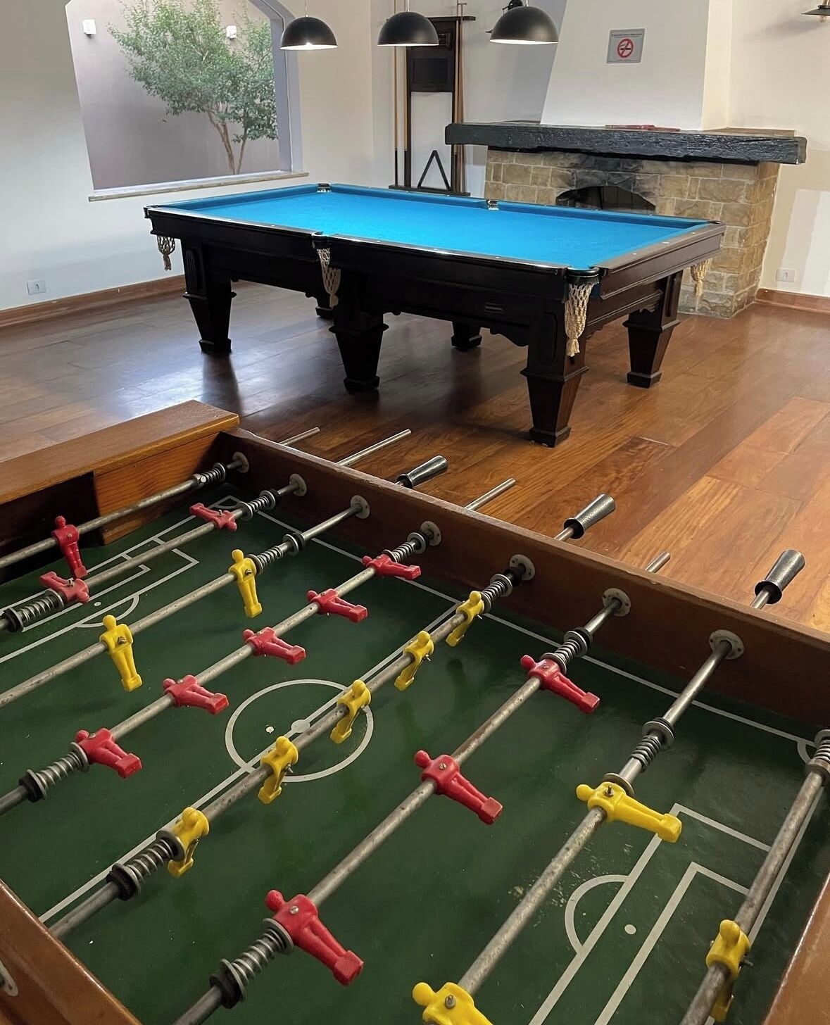 A pool table with a blue felt surface and a foosball table with red and yellow players.