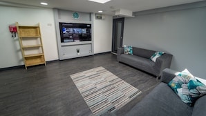 Un salon moderne avec un canapé gris, une échelle en bois, un téléviseur à écran plat et une lucarne.