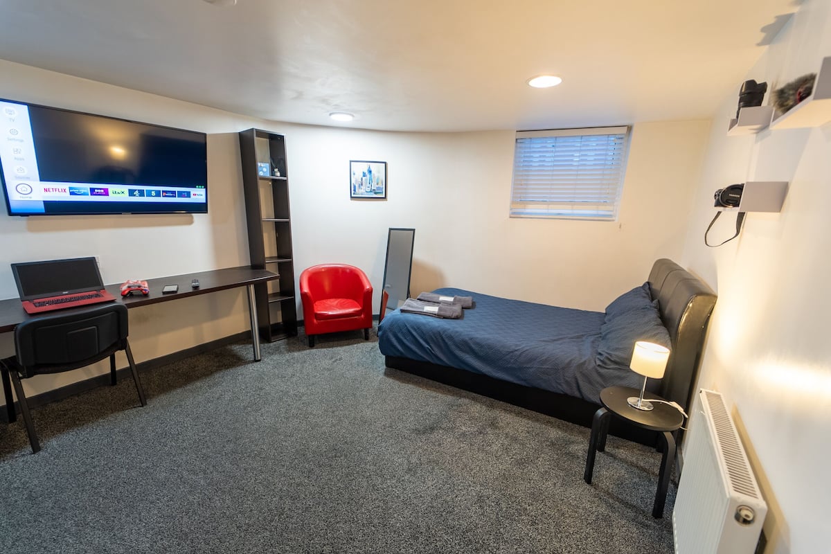 Une chambre d’hôtel compacte comprenant un lit, un bureau avec un ordinateur portable, une chaise rouge, un téléviseur fixé au mur et un radiateur.